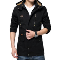 A man wearing a black hooded winter jacket with a tan faux-fur lined hood, front zipper, and flap pockets, paired with a white t-shirt and blue jeans against a light gray background.
