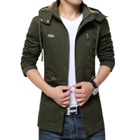 A man wearing an olive green hooded jacket with a brown faux-fur collar, layered over a white t-shirt and blue jeans.