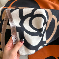 Close-up of a patterned fabric with a hand holding it, against an orange and black background.