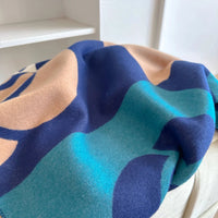 Close-up of a colorful fabric with blue, green, and beige patterns on a white surface.